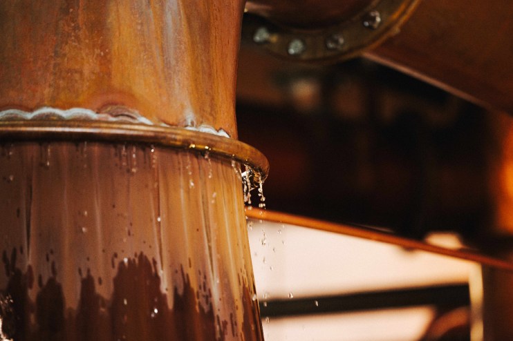 Close-up of water dripping from the copper cooling ring of a Fettercairn whisky still.