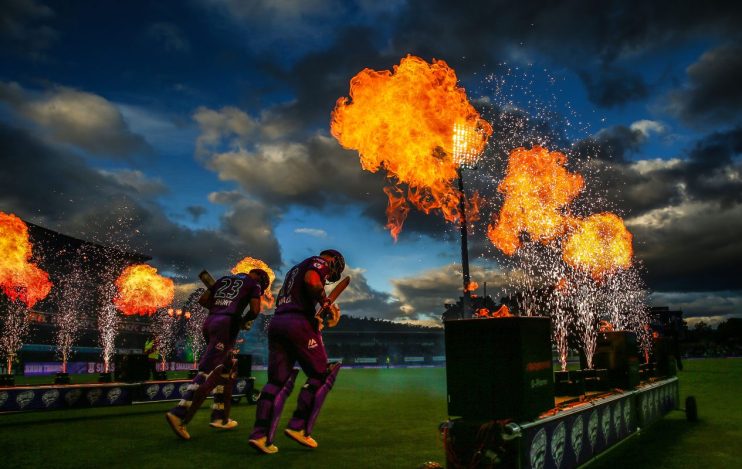 Cricket players DArcy Short and Matthew Wade walk onto the field amidst fire and fireworks at dusk.