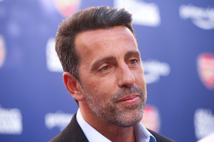 Close-up of a man with salt-and-pepper hair and beard, wearing a suit, against a blurred blue background.