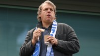 Todd Boehly, Chelsea FC co-owner, eating a snack and holding a cup, wearing a gray coat and blue scarf.