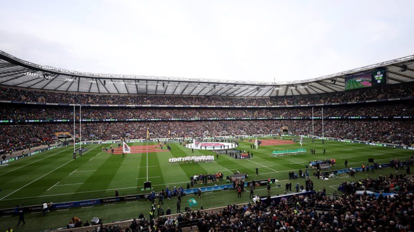 Rugby players on the field with a packed stadium, England vs. Ireland match displayed on screens.