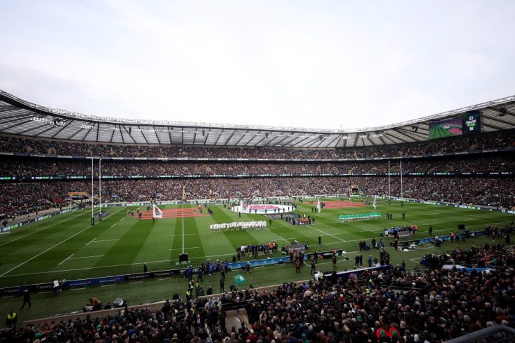 Rugby players on the field with a packed stadium, England vs. Ireland match displayed on screens.