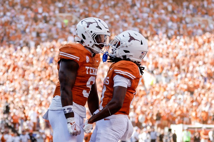 Two college football players in orange and white uniforms celebrate on a field with a crowd in the background