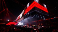 Formula 1 75th anniversary celebration event with F1 cars and drivers on stage, surrounded by red lights and a crowd
