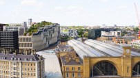 Aerial view of Kings Cross Station in London with modern buildings, a green roof, and a construction crane.