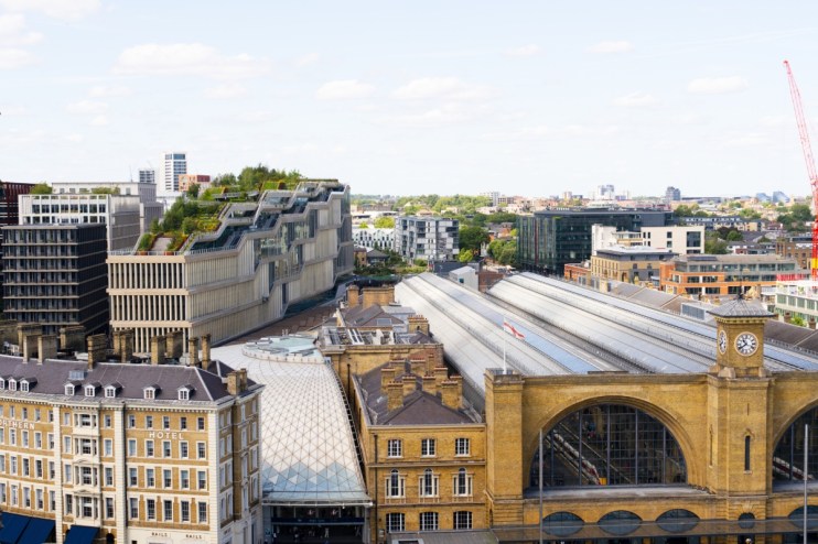 Aerial view of Kings Cross Station in London with modern buildings, a green roof, and a construction crane.