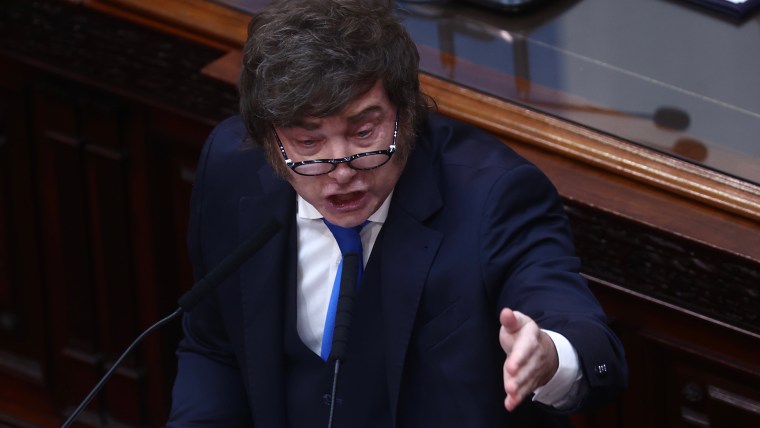 Javier Milei speaking passionately at a podium, gesturing with his right hand, in a formal setting.