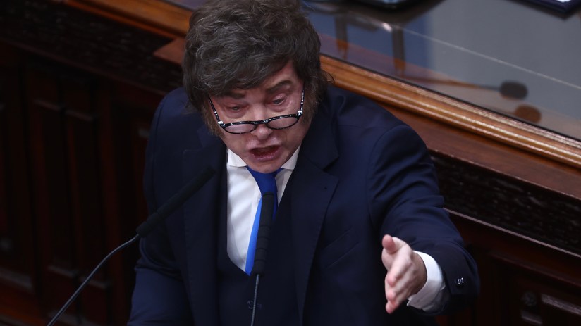 Javier Milei speaking passionately at a podium, gesturing with his right hand, in a formal setting.