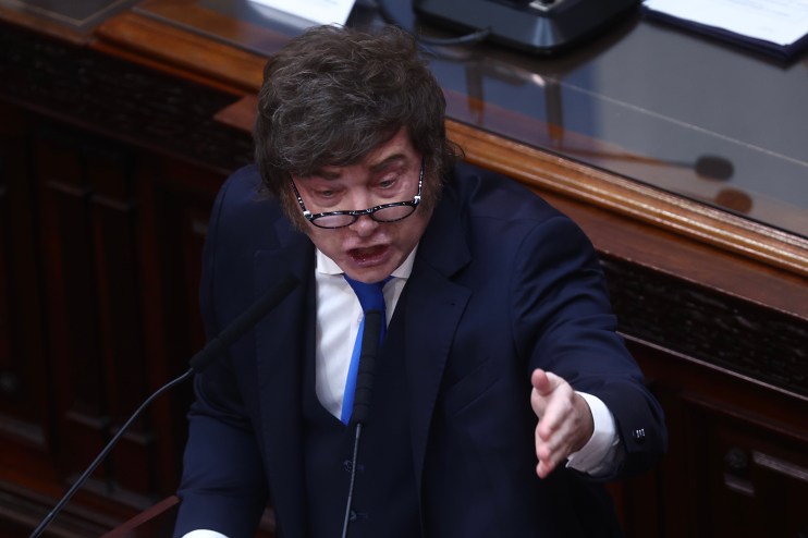 Javier Milei speaking passionately at a podium, gesturing with his right hand, in a formal setting.
