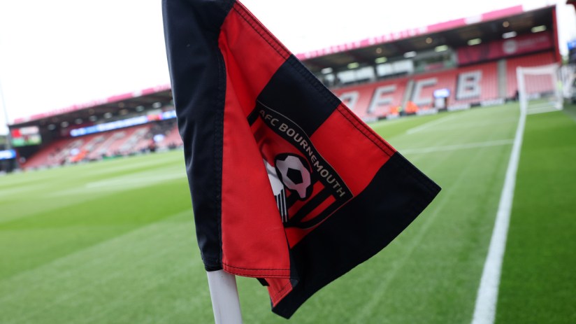AFC Bournemouth corner flag with team logo, vibrant green pitch, and stadium seating in the background.