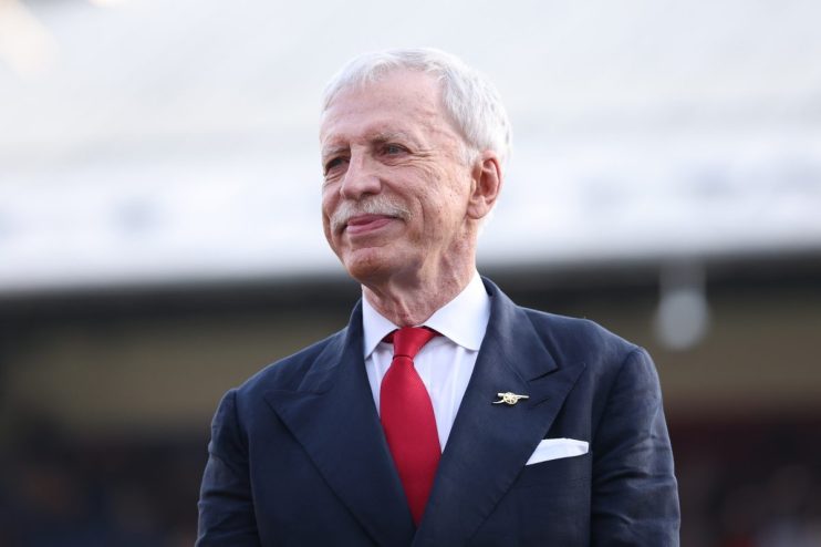 Stan Kroenke, Arsenal Football Club owner, smiling in a navy suit with a red tie and Arsenal pin.