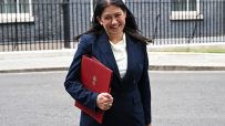 Michelle Donelan, Secretary of State, smiling and holding a red folder outside a building