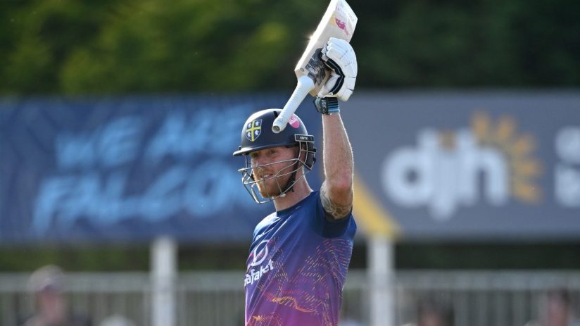 Ben Stokes, in batting gear, raises his cricket bat in celebration on the field.