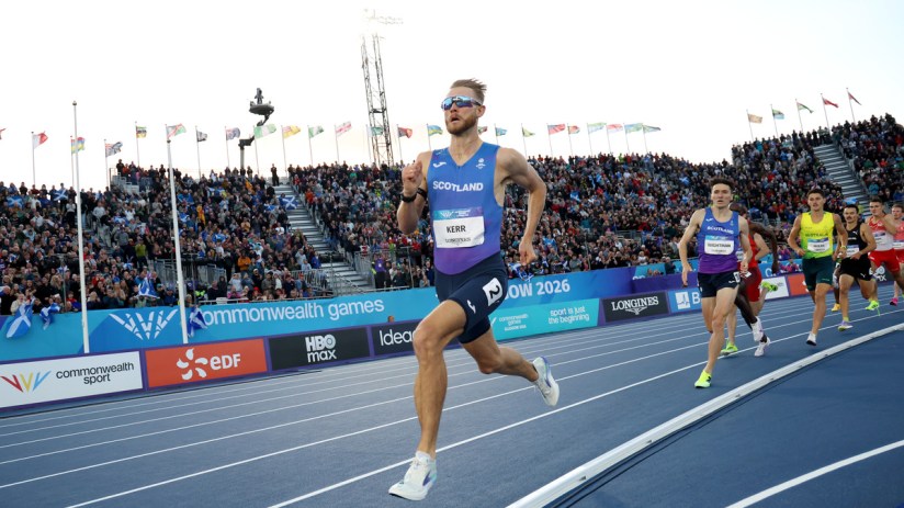 Jake Wightman and other male athletes compete in a track event at the Commonwealth Games, with spectators in the stands.