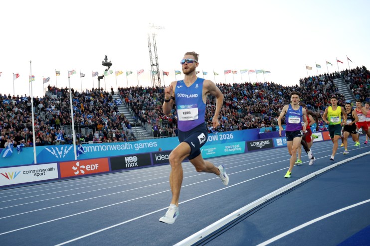 Jake Wightman and other male athletes compete in a track event at the Commonwealth Games, with spectators in the stands.