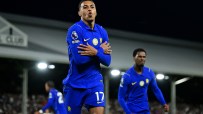 Footballer in blue jersey with arms crossed, celebrating a goal on the field at night with other players in background