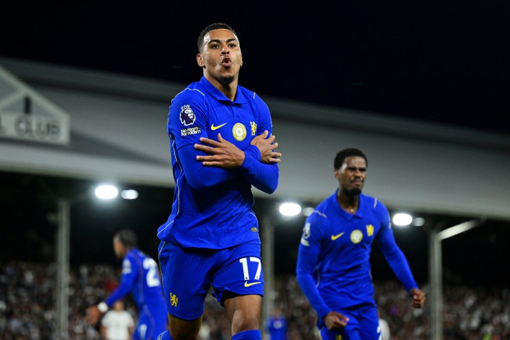Footballer in blue jersey with arms crossed, celebrating a goal on the field at night with other players in background