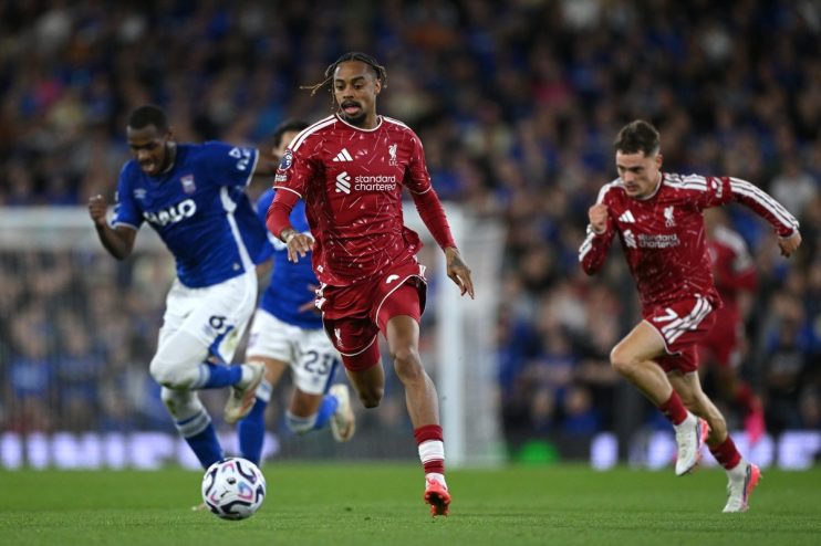 Liverpool FC players in red uniforms run on a soccer field during a match, with opponents in blue.