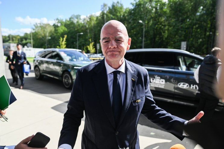 Gianni Infantino, FIFA President, in a navy suit and tie, speaking outdoors with cars and trees in the background.