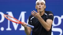 Tennis player Taylor Fritz, wearing a BOSS headband and black shirt, holding a red tennis racket.