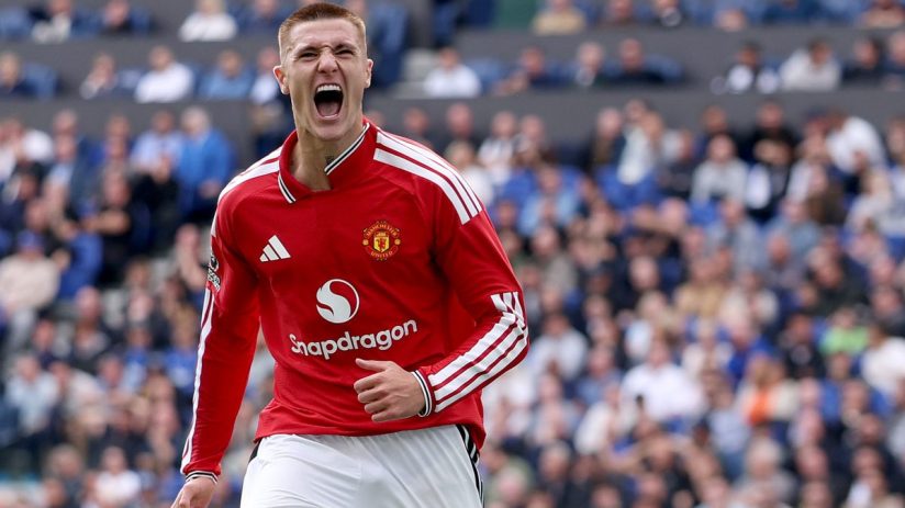 Footballer in Manchester United kit celebrating on the field with a stadium crowd in the background