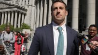 Man in a suit and tie speaks into a CNBC microphone outside a courthouse with large columns.