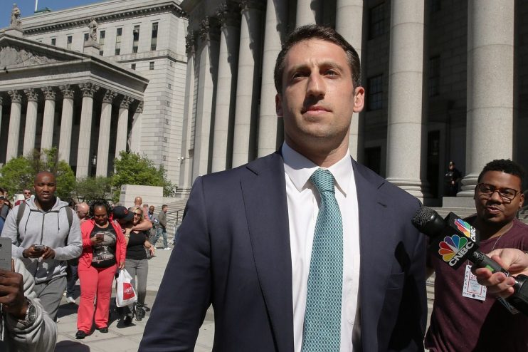 Man in a suit and tie speaks into a CNBC microphone outside a courthouse with large columns.