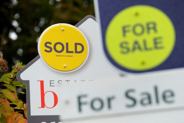 Real estate signs: a yellow SOLD sign and a blurred green FOR SALE sign, indicating house prices and market activity.