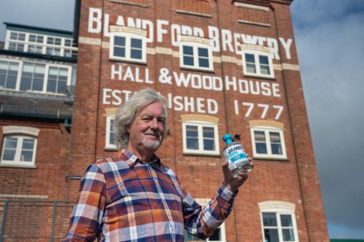 James May holding a bottle of James Gin in front of Blandford Brewery, Hall & Woodhouse established 1777.