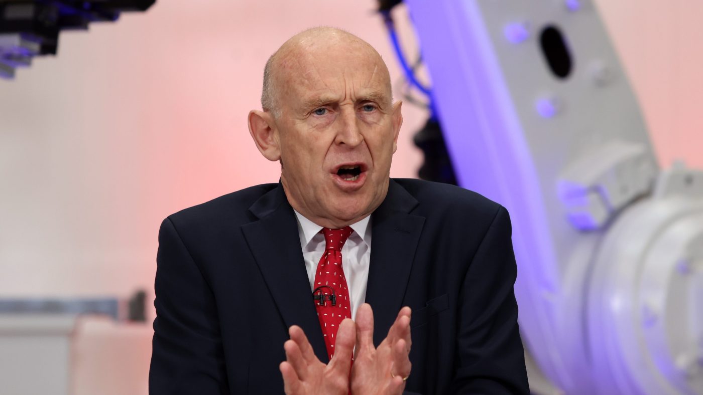 John Healey speaking at JLR, with industrial robotic arms visible in the background