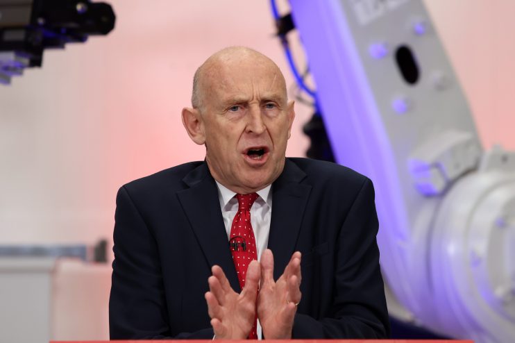 John Healey speaking at JLR, with industrial robotic arms visible in the background