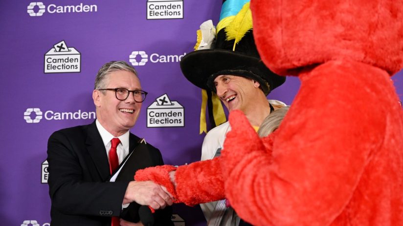 Keir Starmer shaking hands with a man in a tall hat and red furry costume at a Holborn and St Pancras election event.