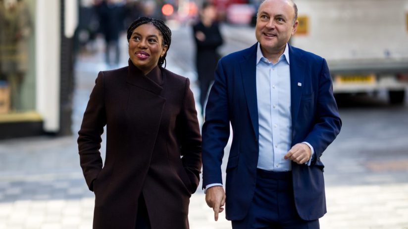 Kemi Badenoch and Andrew Griffith walking together on a city street, smiling.