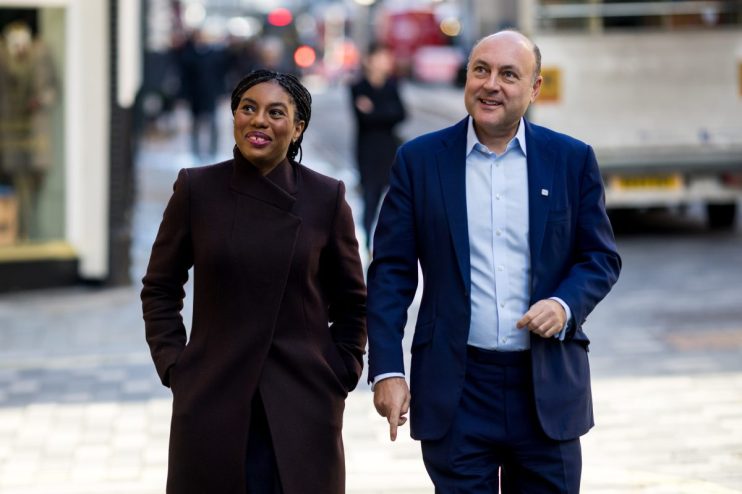 Kemi Badenoch and Andrew Griffith walking together on a city street, smiling.