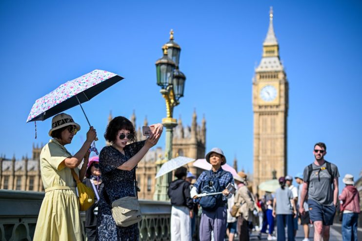Tourists on Westminster Bridge, London, with Big Ben and Houses of Parliament in the background on a sunny day.