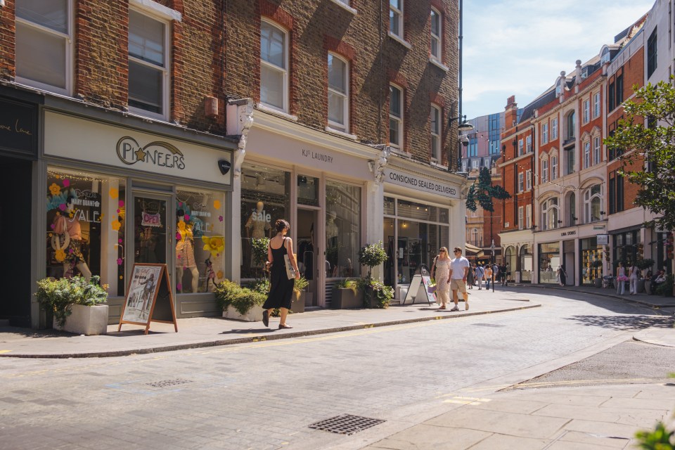 Sunny street scene in Marylebone Village with people walking past shops and brick buildings.