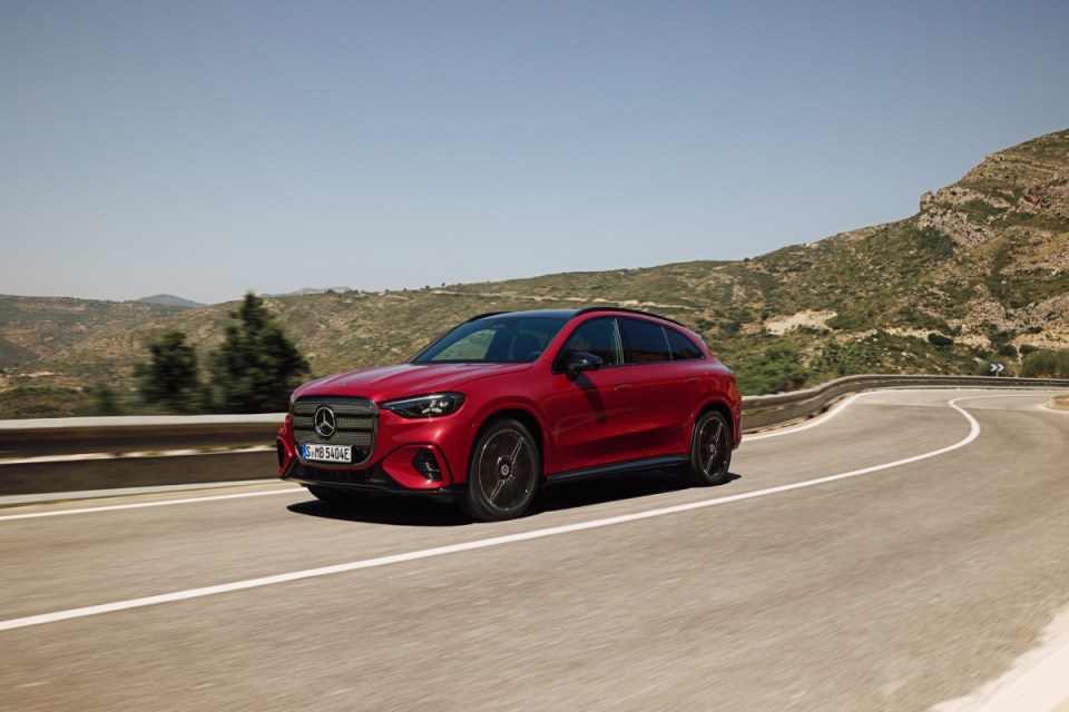 Red Mercedes GLC SUV driving on a winding road with mountains in the background