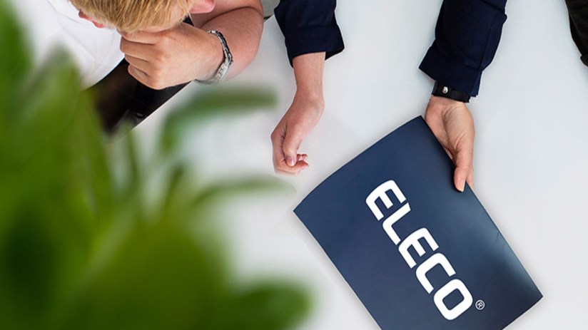 Overhead view of two professionals at a table, one holding a blue folder with the white ELECO logo.