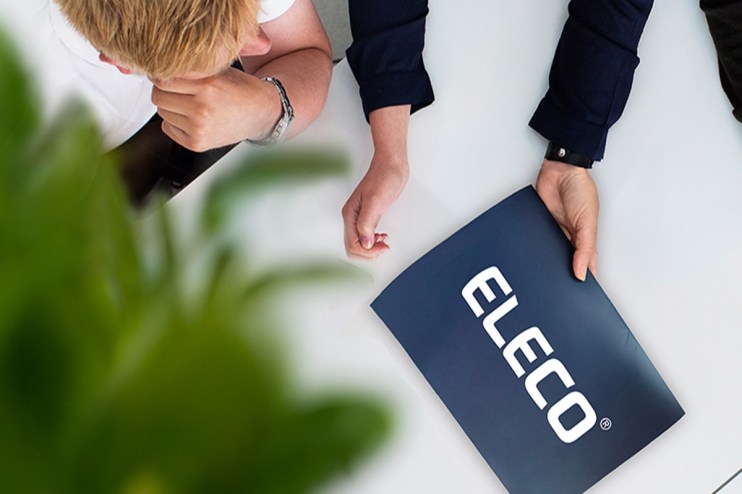 Overhead view of two professionals at a table, one holding a blue folder with the white ELECO logo.