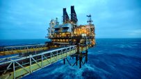 Offshore oil rig platform with illuminated facilities and a long gangway over choppy North Sea waters.