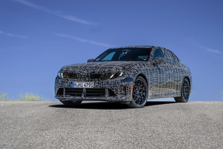 Camouflaged BMW sedan prototype with black and white pattern on an asphalt road under a clear blue sky