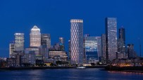 Canary Wharf skyline at dusk with illuminated skyscrapers reflecting in the dark water of the River Thames.