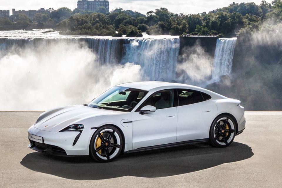 White Porsche Taycan Turbo S electric sports car parked in front of Niagara Falls, showcasing its sleek design.