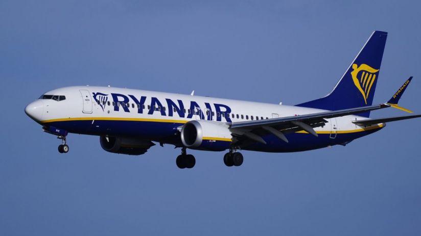 Ryanair Boeing 737 aircraft in flight with landing gear extended against a clear blue sky