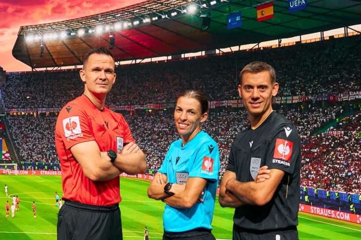 Three football referees, two men and one woman, stand before a large screen displaying a stadium and UEFA Strauss logos.