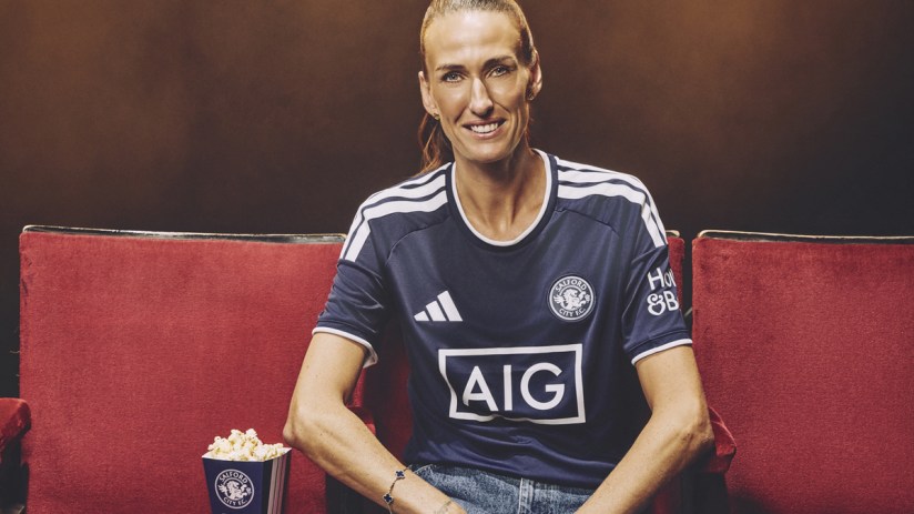 Jill Scott in Salford City FC kit, smiling, sitting on a red seat with popcorn.