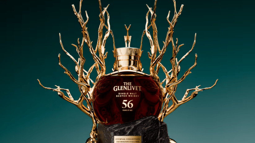 The Glenlivet 56-year-old single malt scotch whisky bottle on a black stone pedestal with gold branch-like accents.