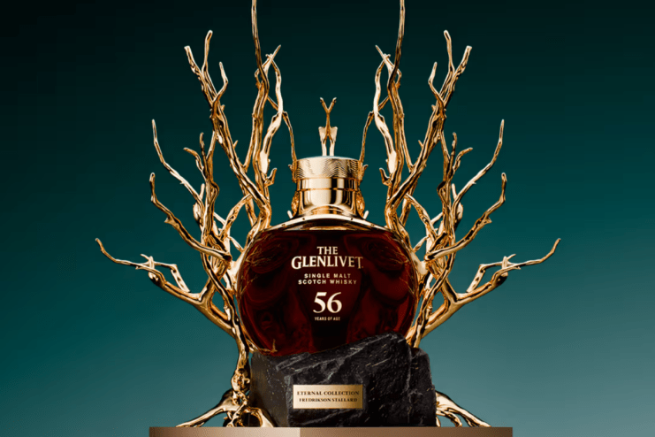 The Glenlivet 56-year-old single malt scotch whisky bottle on a black stone pedestal with gold branch-like accents.