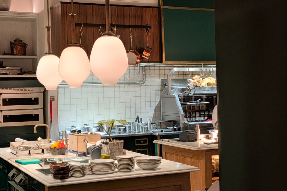 A modern, well-lit Six Senses kitchen with white tile backsplash, commercial ovens, and hanging copper pots