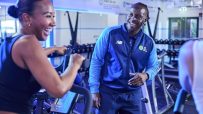 Man in The Gym Group uniform smiling at a woman on an exercise bike.